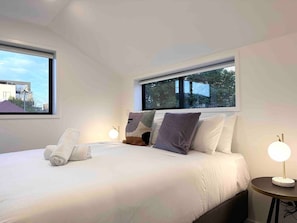 Un dormitorio moderno con una cama grande, dos lámparas de noche y un ventanal con vistas a edificios.