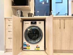 Una unidad compacta de lavadora y secadora con etiquetas de eficiencia energética, ubicada en un gabinete de madera con un ventanal en la parte superior.