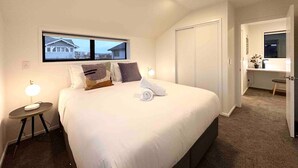 Quarto de hotel com cama grande, luminárias de cabeceira, janela com vista, escrivaninha e guarda-roupa.