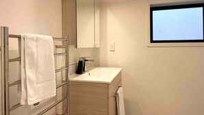 Uma casa de banho moderna com cabine de duche em vidro, lavatório branco e um espelho grande sobre a cómoda.