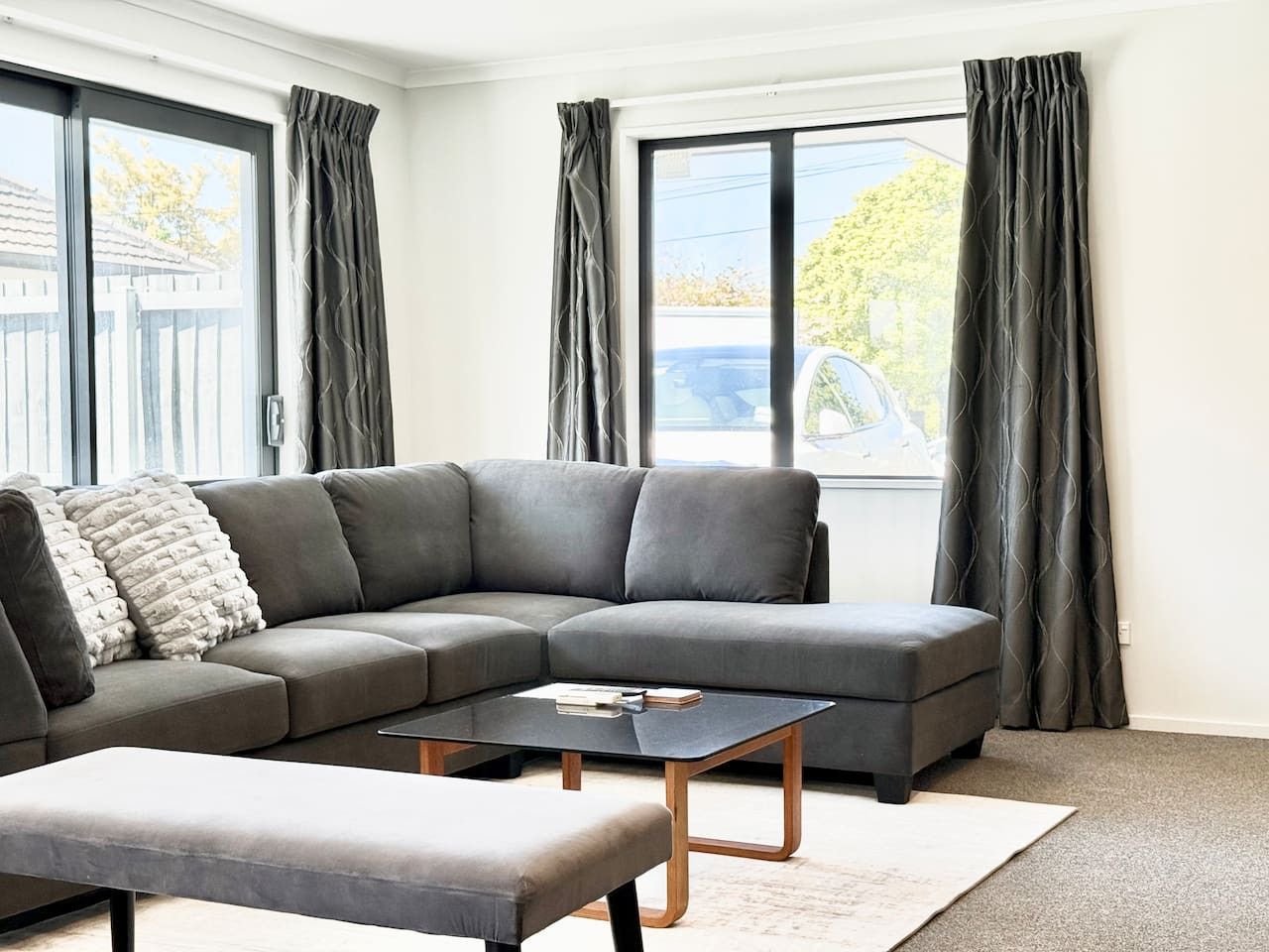 En moderne stue med en grå hjørnesofa, et lille sofabord og en grå skammel.