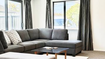 En moderne stue med en grå hjørnesofa, et lille sofabord og en grå skammel.