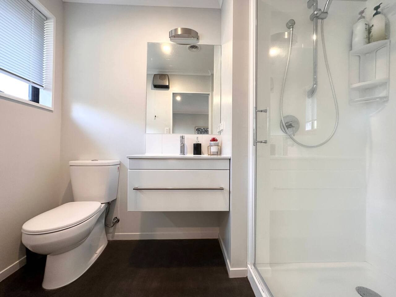 Une salle de bain moderne comprenant des toilettes, un meuble-lavabo avec un miroir et une douche à l’italienne.