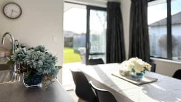 A modern kitchen with a dining area, a clock on the wall, and a view of the outdoors.