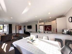 Uma cozinha moderna com uma ilha central, área de jantar com mesa e cadeiras, sofá e televisão de tela plana na parede.