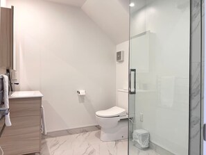 A modern bathroom with a toilet, a glass shower enclosure, and a wooden vanity. - Cashel townhouse with courtyard and baby gear in Christchurch (Christchurch)