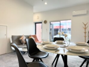 A dining area with a round table set for four, black chairs, and a sofa in the background. - Cashel townhouse with courtyard and baby gear in Christchurch (Christchurch)