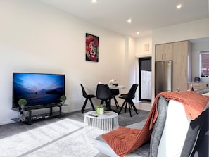 A modern living room with a flat-screen TV, a dining table with chairs, a coffee table, and a sofa with a throw blanket.