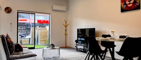 A modern living room with a sofa, a coffee table, and a dining area with chairs and a TV.