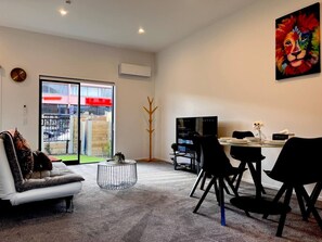 A modern living room with a sofa, a coffee table, and a dining area with chairs and a TV.