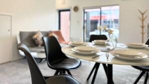 Un coin repas avec une table ronde dressée pour quatre personnes, des chaises noires et un canapé en arrière-plan.