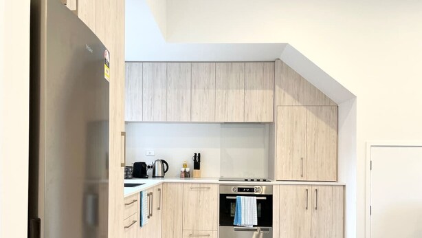 Une cuisine moderne avec des meubles en bois clair, des appareils en acier inoxydable et un four encastré.