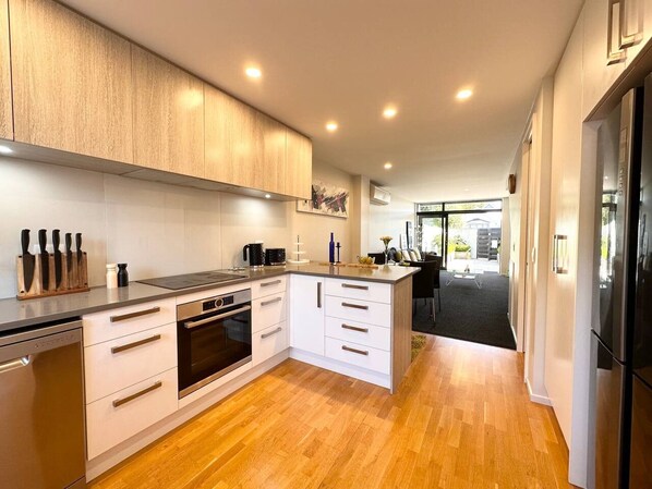 A modern kitchen with white cabinetry, stainless steel appliances, and a wooden floor.