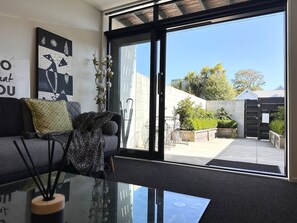 A modern living room with a sofa, decorative pillows, a glass coffee table, and a view of the outdoor area through large sliding doors. - Peacock townhouse with garage and balcony in Christchurch (Christchurch)