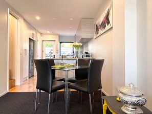 Un comedor moderno con una mesa y sillas, un jarrón con flores y una urna de plata decorativa sobre una mesita auxiliar.
