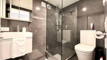 A modern bathroom with a glass-enclosed shower, a white toilet, and a vanity with a mirror and storage.