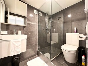 A modern bathroom with a glass-enclosed shower, a white toilet, and a vanity with a mirror and storage. - Peacock townhouse with garage and balcony in Christchurch (Christchurch)