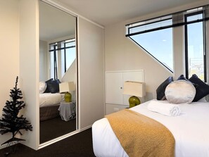 A hotel room with a bed, a large mirror, a small Christmas tree, and a window with blinds.