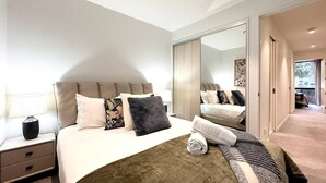 A modern bedroom with a large bed, a nightstand, a mirror, and a view of a balcony.