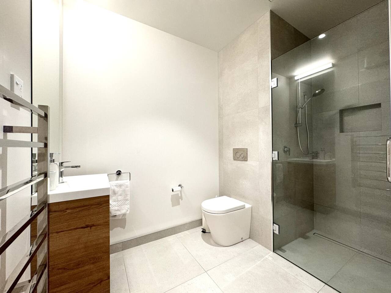 Een moderne badkamer met een douchecabine van glas, een houten wastafelmeubel en een wit toilet.