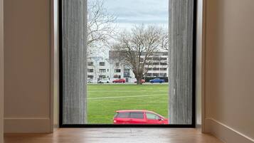 A room with a wooden floor and a view through a glass door to a grassy area with a red car and buildings in the background.