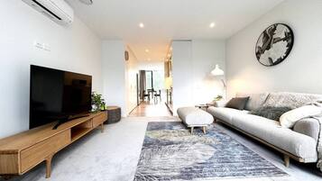 Ein modernes Wohnzimmer mit Flachbildfernseher, einer Couch, einem Couchtisch und einem gemusterten Teppich.