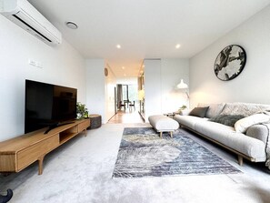 Ein modernes Wohnzimmer mit Flachbildfernseher, einer Couch, einem Couchtisch und einem gemusterten Teppich.