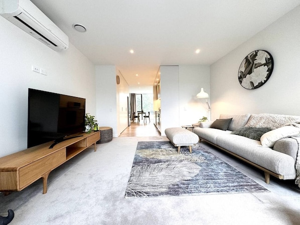 A modern living room with a flat-screen TV, a sofa, a coffee table, and a patterned rug.