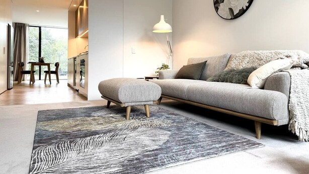 A modern living room with a sofa, ottoman, and a large rug.