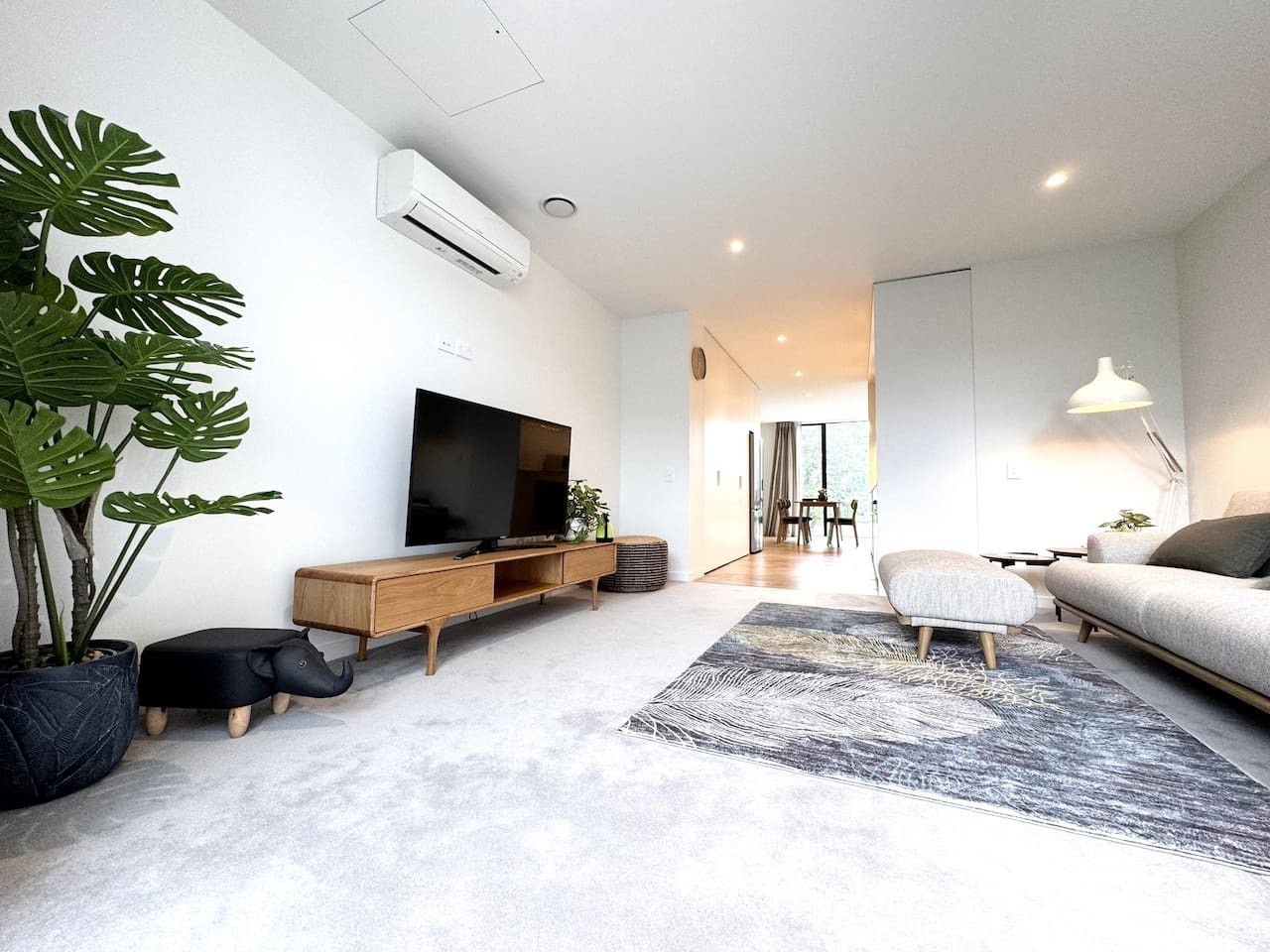 A modern living room with a flat-screen TV, a sofa, a coffee table, and a large potted plant.