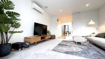 A modern living room with a flat-screen TV, a sofa, a coffee table, and a large potted plant.
