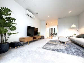Una sala de estar moderna con una televisión de pantalla plana, un sofá, una mesa de centro y una planta grande en maceta.