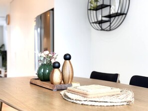 Ein Holztisch mit einer gewebten Tischmatte, einer grünen Vase mit Blumen sowie Holzsalz- und Pfefferschüttlern.