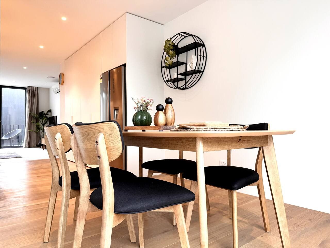 A dining area with a wooden table and chairs, a decorative wall piece, and a view of the room.