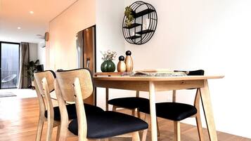 A dining area with a wooden table and chairs, a decorative wall piece, and a view of the room.