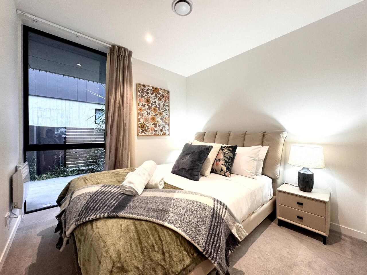 Une chambre à coucher avec un lit, une table de chevet, une lampe et une fenêtre avec des rideaux.