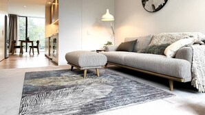 A modern living room with a sofa, ottoman, and a large rug.