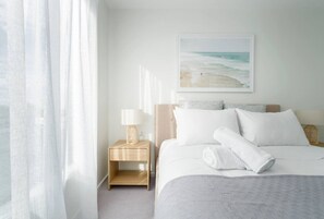 A hotel room with a bed, a nightstand with a lamp, a beach view painting, and sheer curtains. - Cashel penthouse with city balcony and parking in Christchurch (Christchurch)