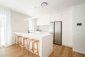 Eine moderne Küche mit weißen Schränken, einem Edelstahlkühlschrank und Holzhockern.