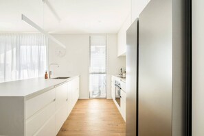 A modern kitchen with white cabinetry, a wooden floor, and a stainless steel refrigerator. - Luxury Penthouse in City Private central live (Christchurch)