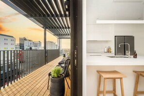 A modern apartment with a balcony, a kitchen with white cabinets, and a stainless steel refrigerator.