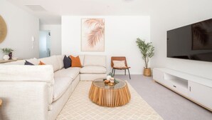 A modern living room with a sectional sofa, a coffee table, a TV, and a large plant. - Cashel penthouse with city balcony and parking in Christchurch (Christchurch)