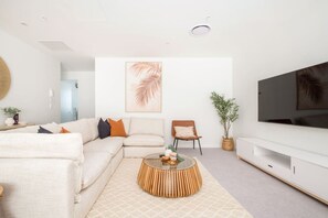 A modern living room with a sectional sofa, a coffee table, a TV, and a large plant. - Luxury Penthouse in City Private central live (Christchurch)
