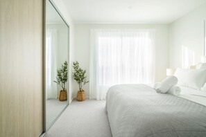 Une chambre d’hôtel moderne avec un grand lit, un miroir et deux plantes en pot.