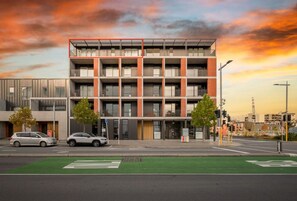 A modern multi-story building with a green bike lane in front, two cars parked on the street, and a sunset sky. - Luxury Penthouse in City Private central live (Christchurch)