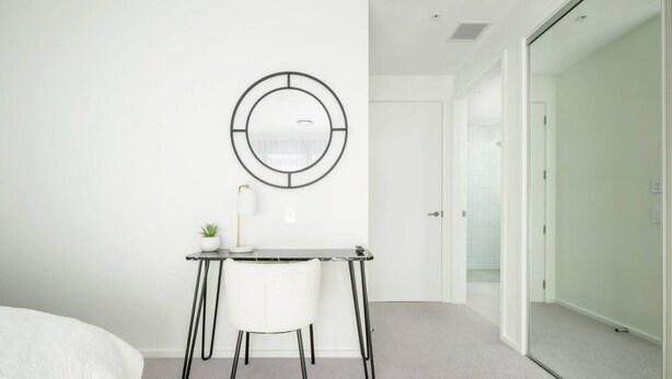 A modern bedroom with a bed, a desk with a chair, a small plant, and a wall-mounted circular mirror. - Cashel penthouse with city balcony and parking in Christchurch (Christchurch)