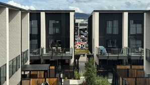 Un edificio moderno con balcones de dos pisos, ventanas amplias y vistas a coches aparcados y montañas al fondo.