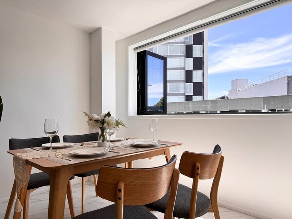 A dining area with a wooden table set for four, two chairs, and a window with a view of buildings.