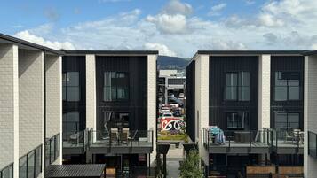 A modern building with two-story balconies, large windows, and a view of parked cars and mountains in the background.