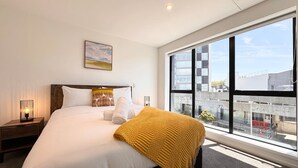 Habitación de hotel con una cama grande, una ventana con vistas a la ciudad, una lámpara de noche y un cuadro en la pared.